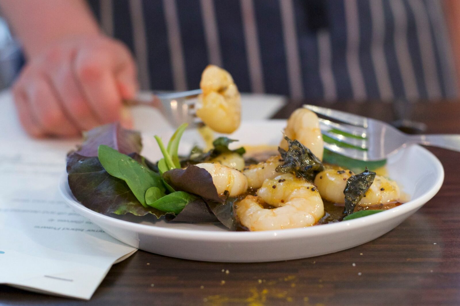 hands holding fork above plate where shripms are served