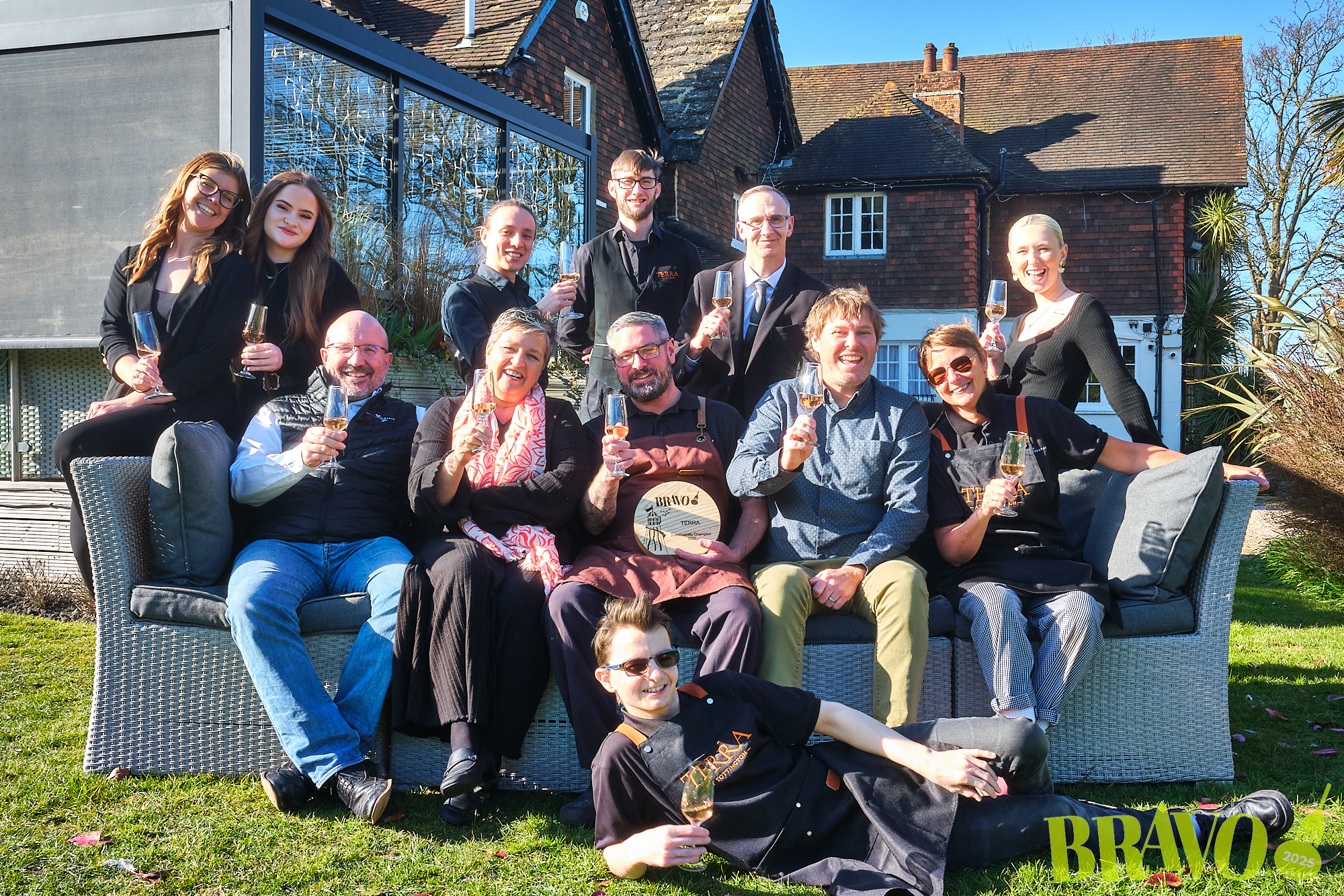 Staff at Terra restaurants, winners of BRAVO Sustainability Champions, holding their trophy and drinking sparkling wine in the susnshine