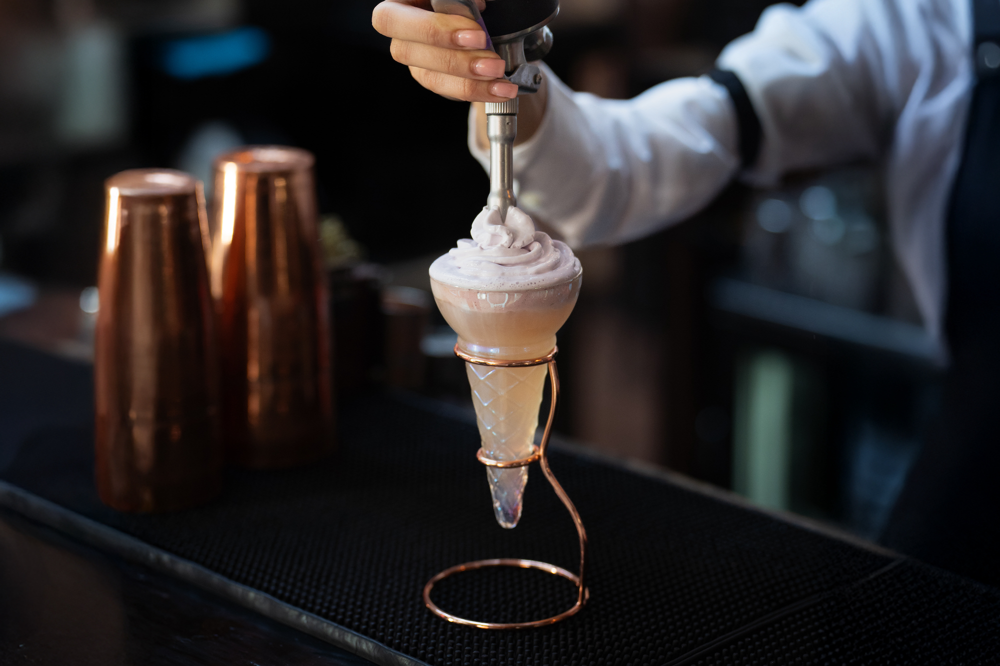A cocktail being created, with cream being piped on top