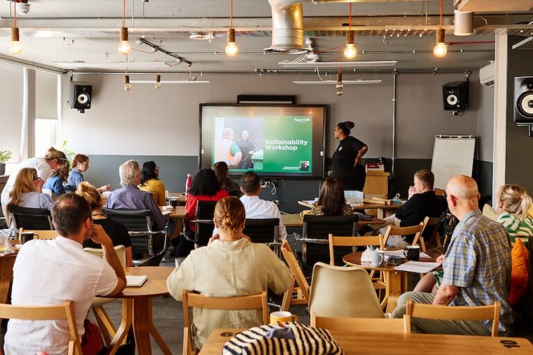 Room of people watching a presentation. We can see a green screen with the words Sustainability Workshop