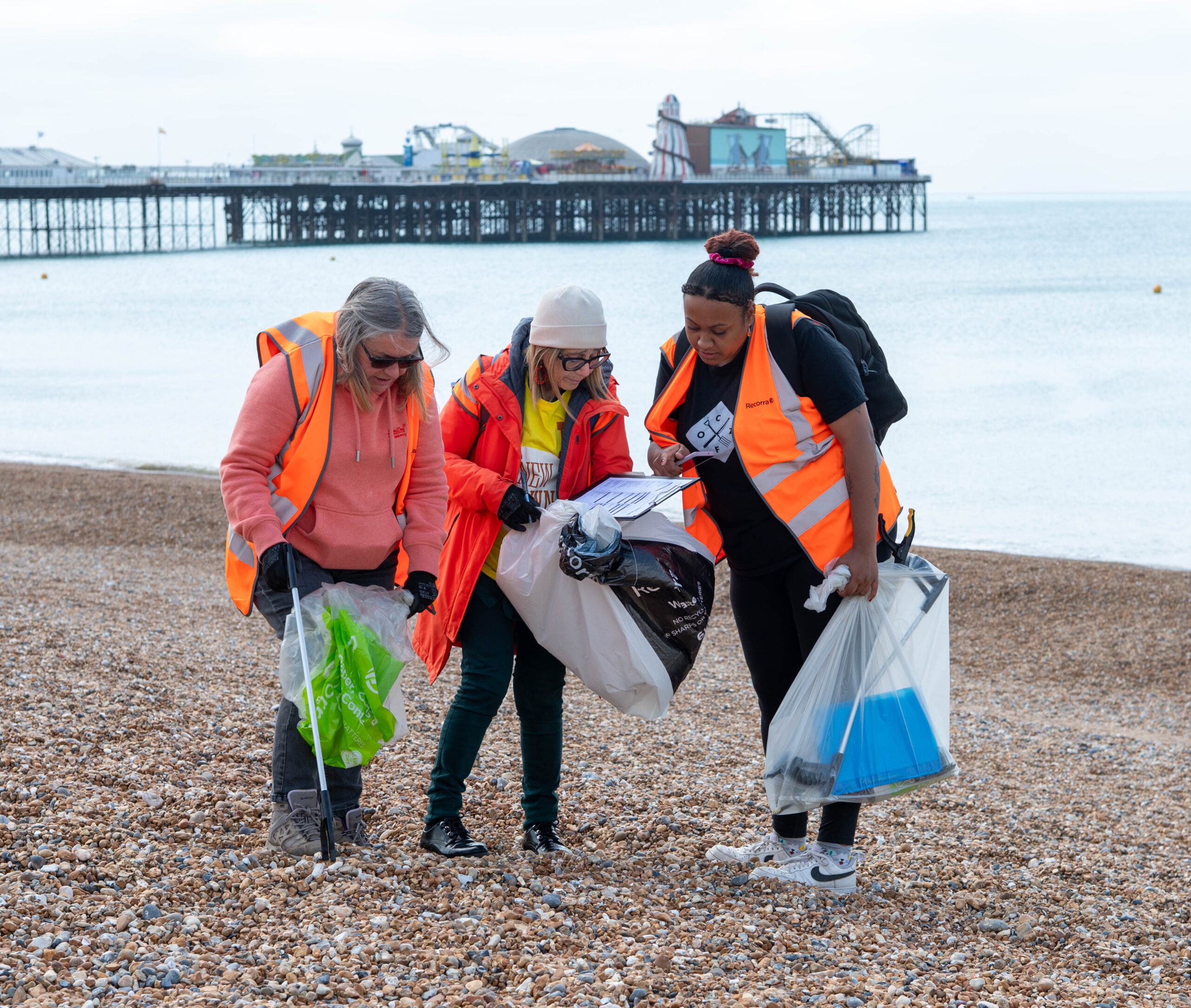 three ladies on the beach collecting plastic bottles 