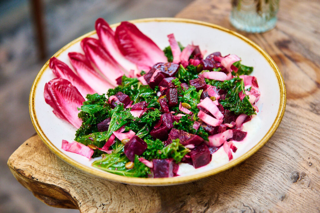 Seasonal beetroot and kale salad with goats cheese on a rustic wooden table.
