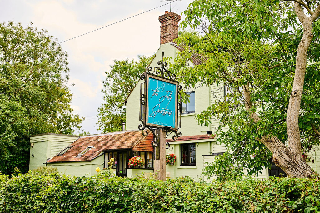 Exterior photo of countryside pub in Sussex on s summer day with lush trees.