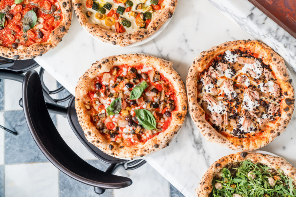 Freshly made pizzas on a marble surface with fresh ingredients and herbs.