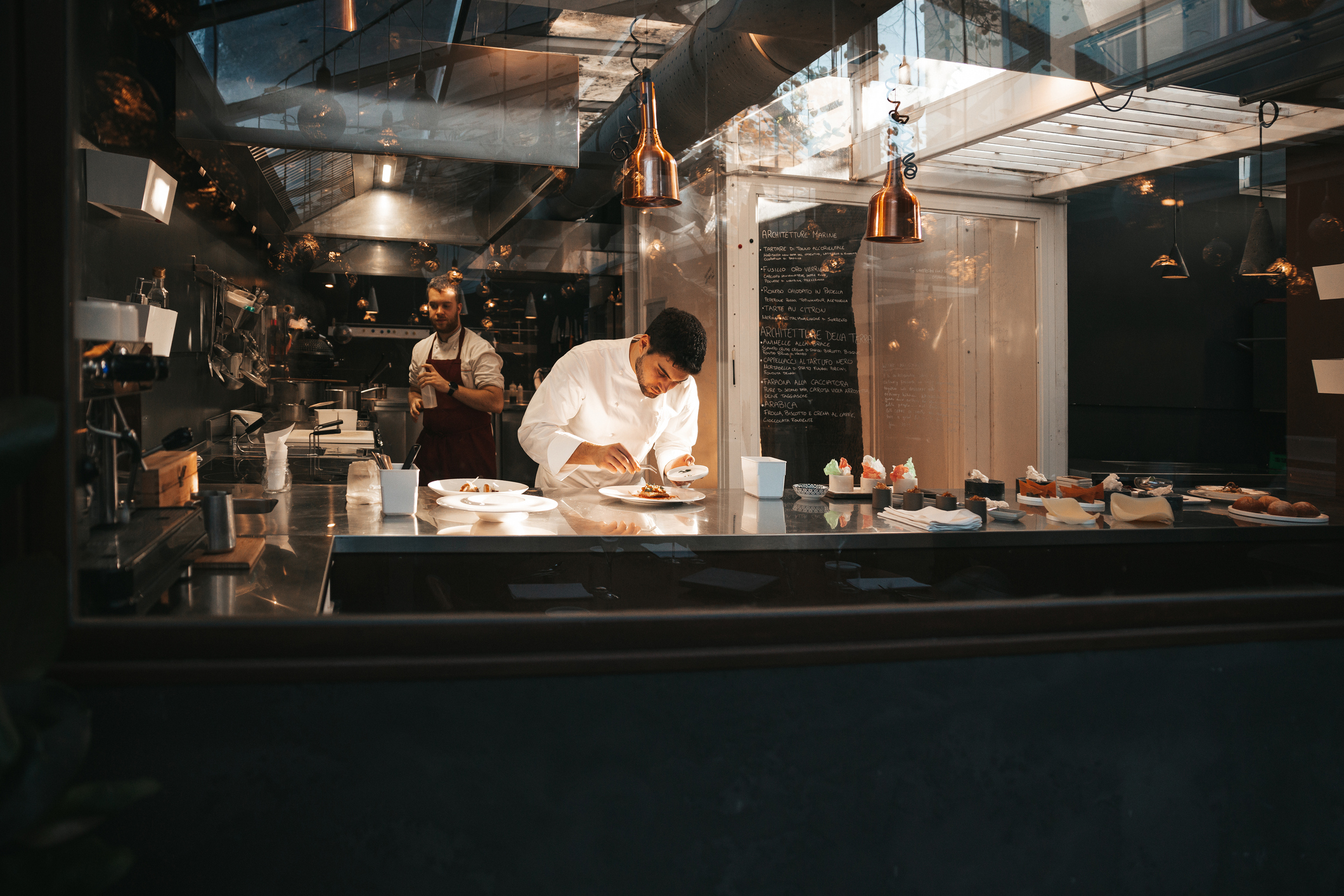 A chef is cooking in his restaurant's kitchen. Shot through the glass. High-end gourmet restaurant.