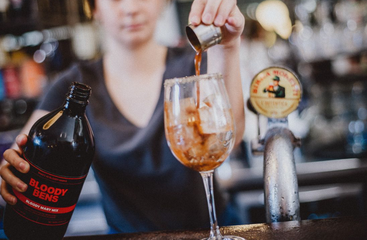 Bartender pouring a measure of spirit into an ice filled glass, holding a bottle in one hand, with a beer tap in the foreground at a Sussex bar.