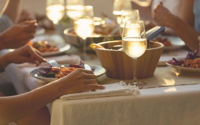 Friends enjoying a meal together on a table at sunset. There is spaghetti Bolognese  and salad on the plates on the table. There are glasses of wine and other food on the table. Tight crop showing only food and hands