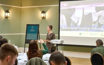 Woman standing by a flip chart in front of a screen with the words sustainability workshop. The slides also show images of chefs.