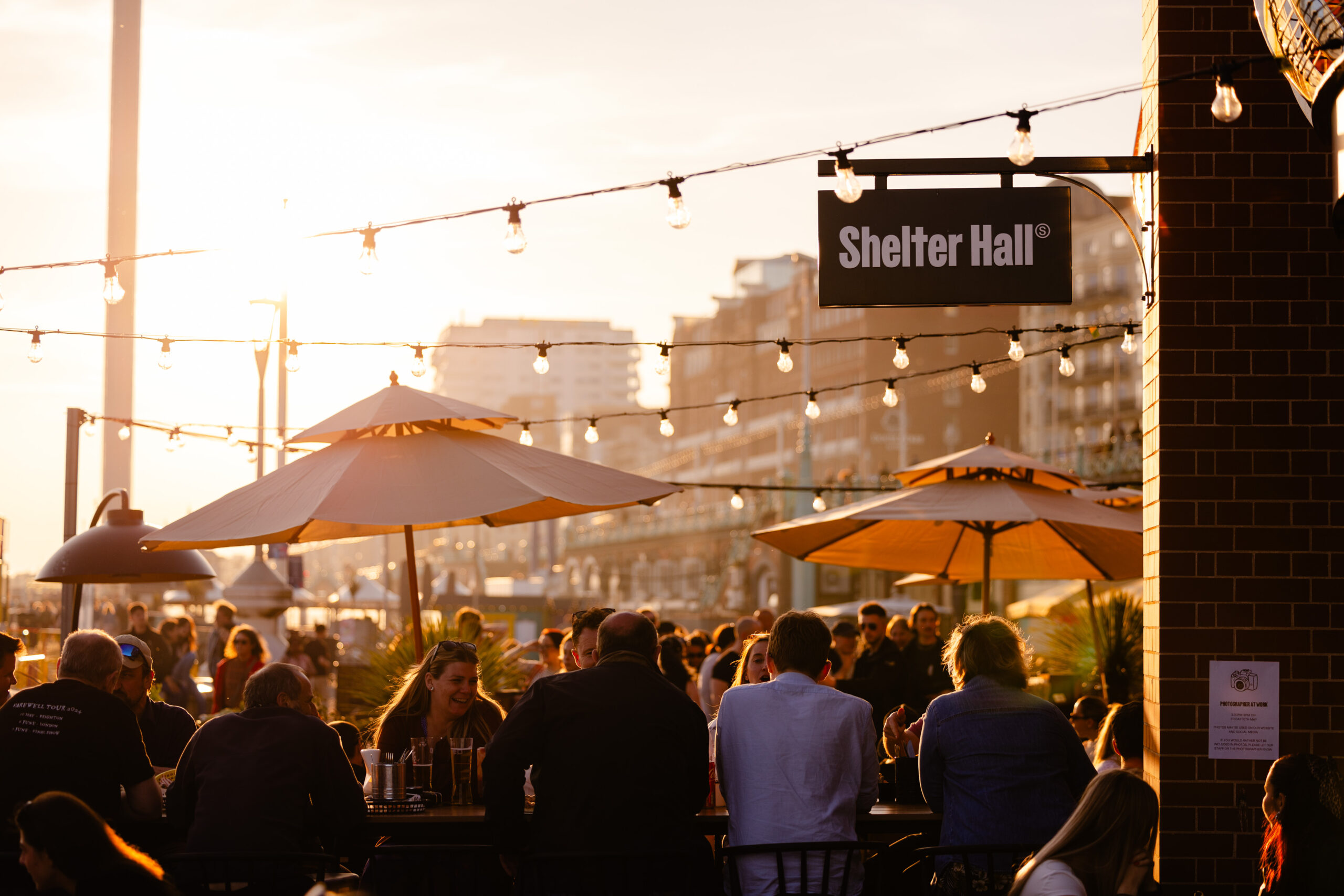 Shelter Hall Brighton, on Brighton Beach UK - shot of people enjoying their drinks and food outside during the sunset. Shelter Hall features as part of the Restaurants in Brighton guide