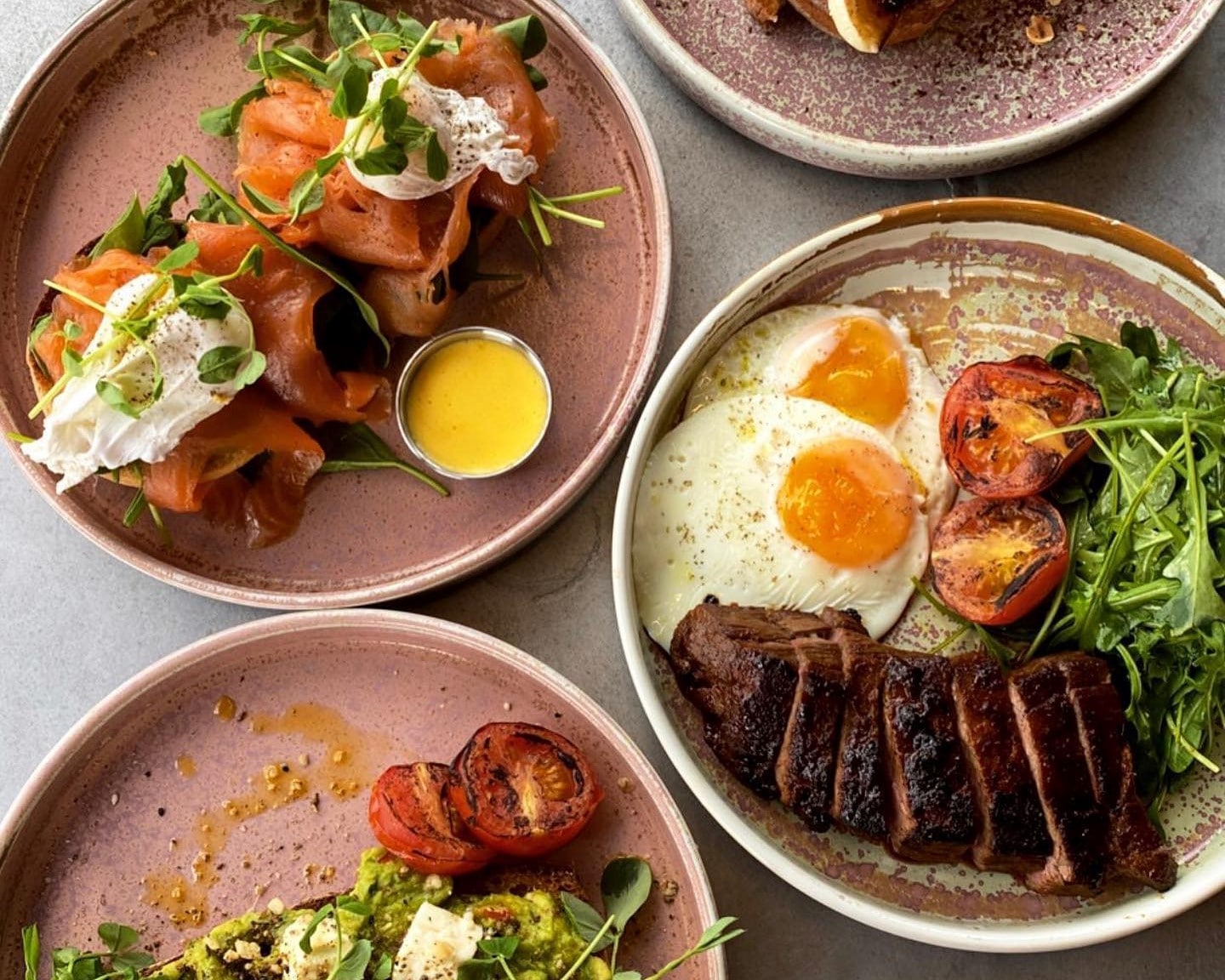 table laid out with few plates including one with eggs, tomates, meat and salad, second with samon and egge and sauce