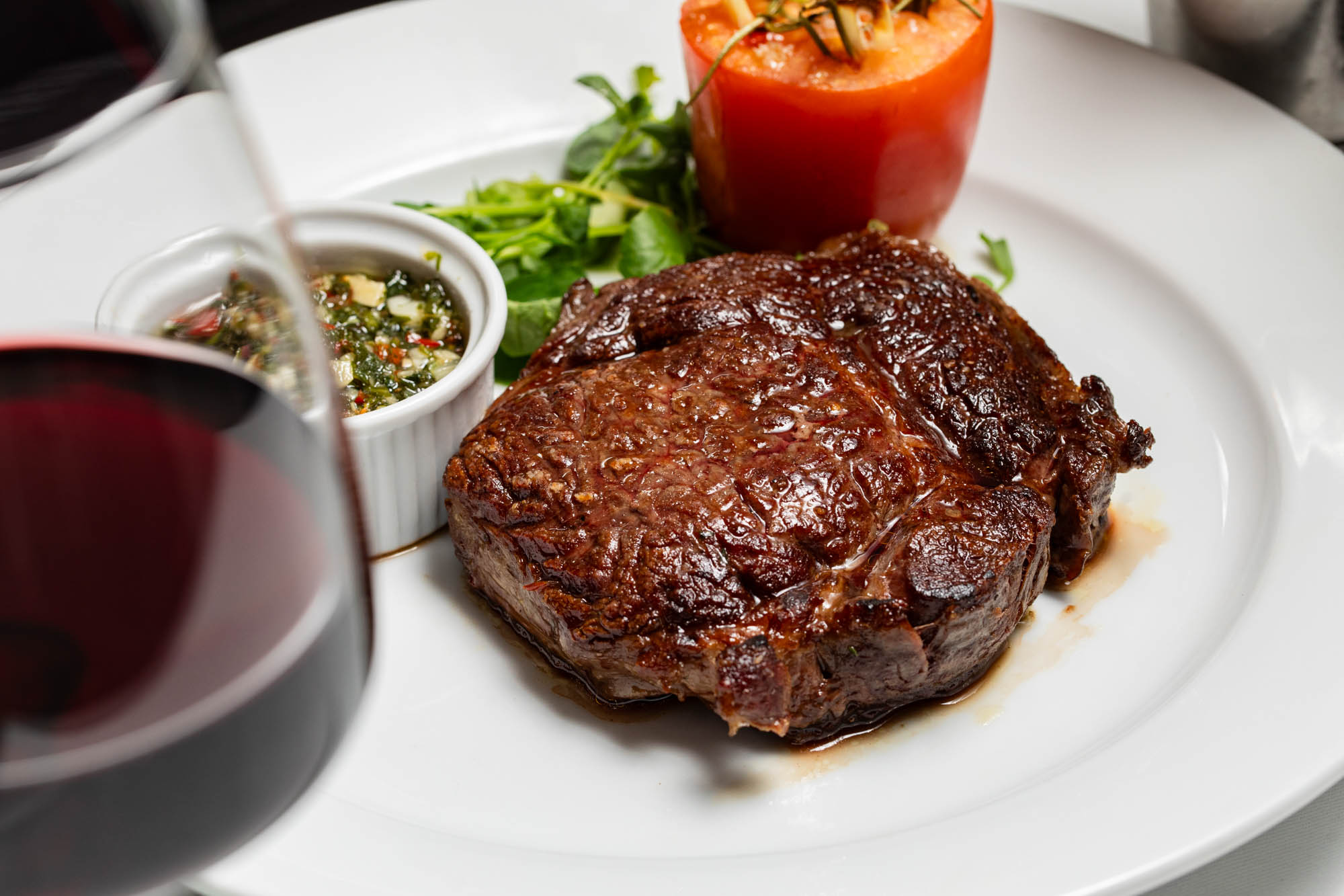 A perfectly seared steak at Il Bistro, served with a side of fresh chimichurri, a roasted tomato, and a garnish of greens. The dish is paired with a glass of rich red wine, making for a classic and indulgent dining experience in the heart of Brighton.