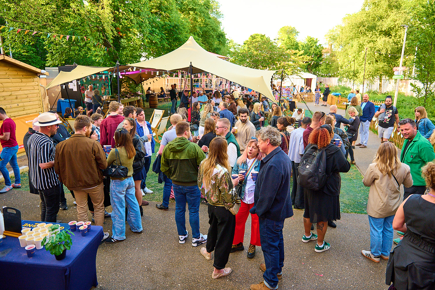 Many people standing around chatting at SpiegelGardens. Lovely green trees frame the picture