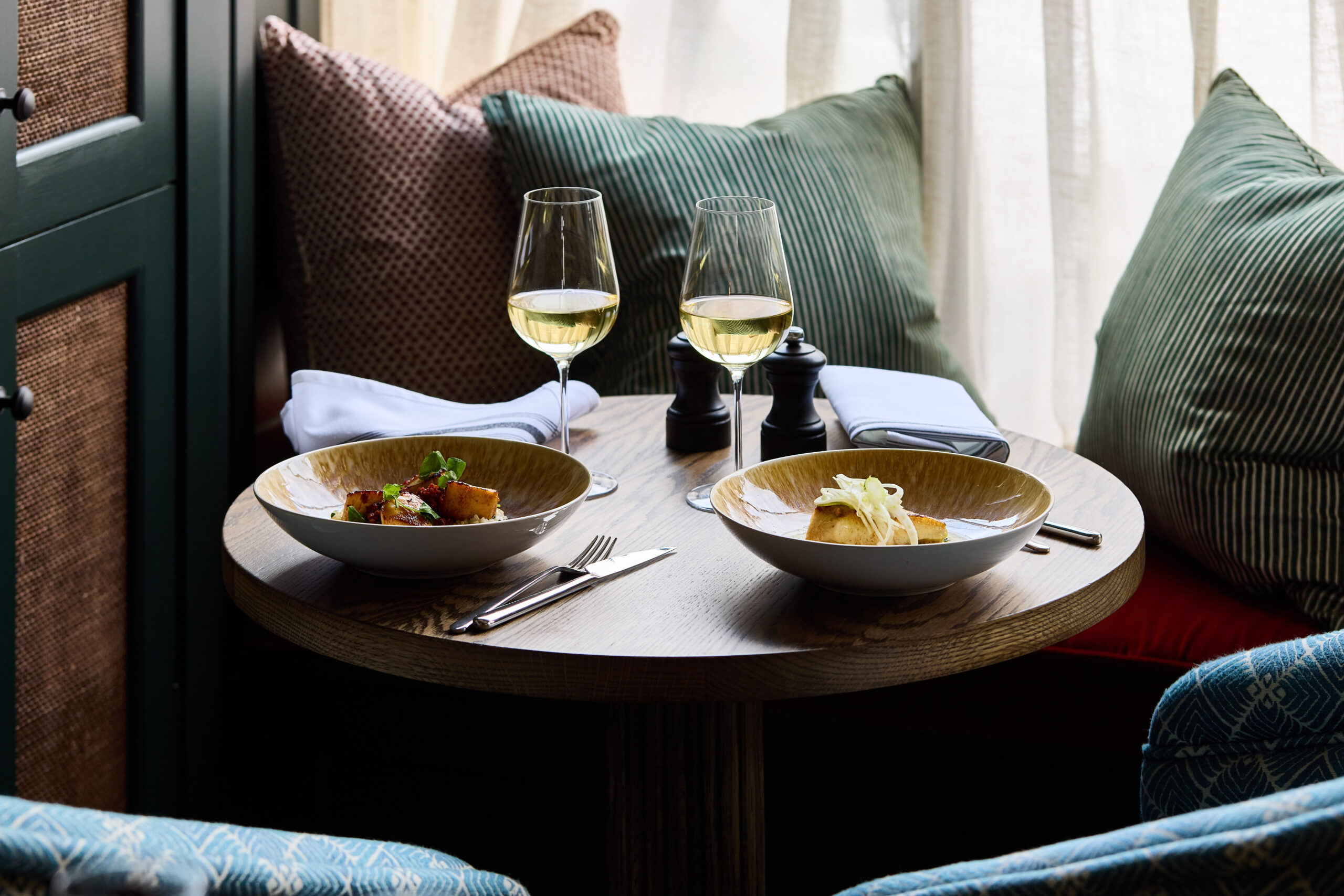 cosy corner of the restaurants, table served with halibut dish with two glasses of white wine