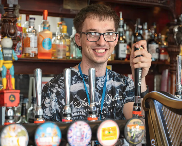 person standing behind a pub bar with their hand on a pump