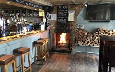 Bar area with wooden bar stools and a roaring wood fire with duck egg blue paint work.