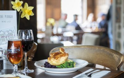 Roast dinner with Yorkshire pudding and wine at the table with a vase of daffodils and people in the background.